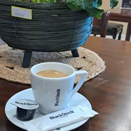 Kopje koffie met BlackStock-logo op schotel met decoratieve objecten op achtergrond