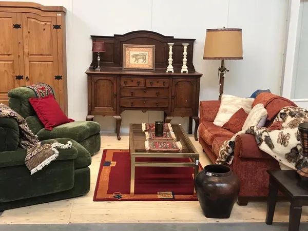 Woonkamer-inrichting met groene en rode fauteuils, houten dressoir, salontafel en diverse meubels en accessoires