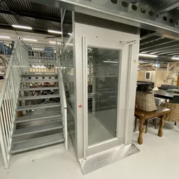 Witte showroom met glazen deuren en witte trap met metalen balustrade, op de achtergrond meubels en spullen uitgestald