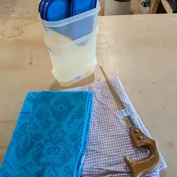 Close-up van huishoudelijke artikelen: blauwe doek, paarse doek, houten lepel en plastic container met water