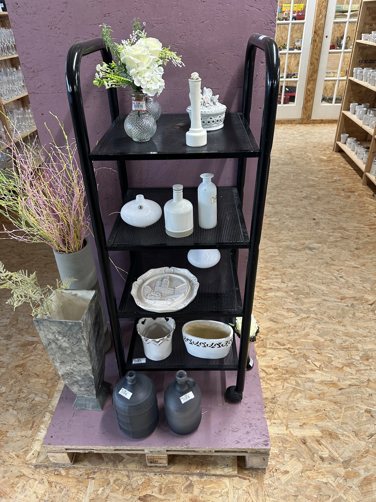 Zwarte stellingkast met wit huishoudelijk servies en decoratieve items uitgestald op verschillende niveaus