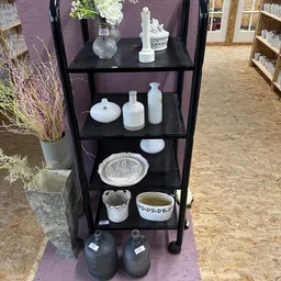 Zwarte stellingkast met wit huishoudelijk servies en decoratieve items uitgestald op verschillende niveaus