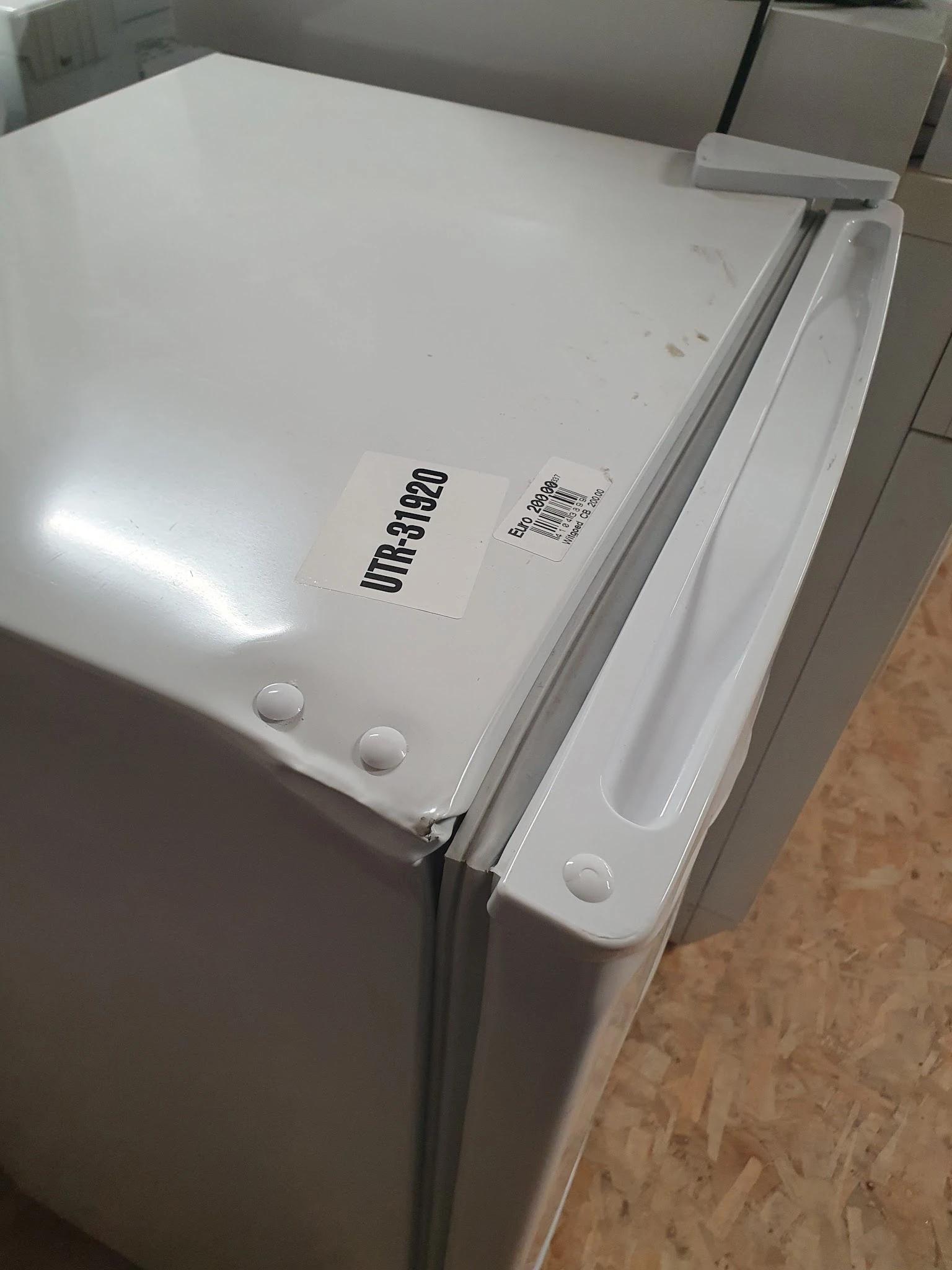 Bovenkant van een witte koelkast met het merk 'Umbro80' en een barcode-etiket