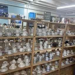 Houten stellingen vol met serviesgoed, kopjes, schotels en ander keramiek in een kringloopwinkel