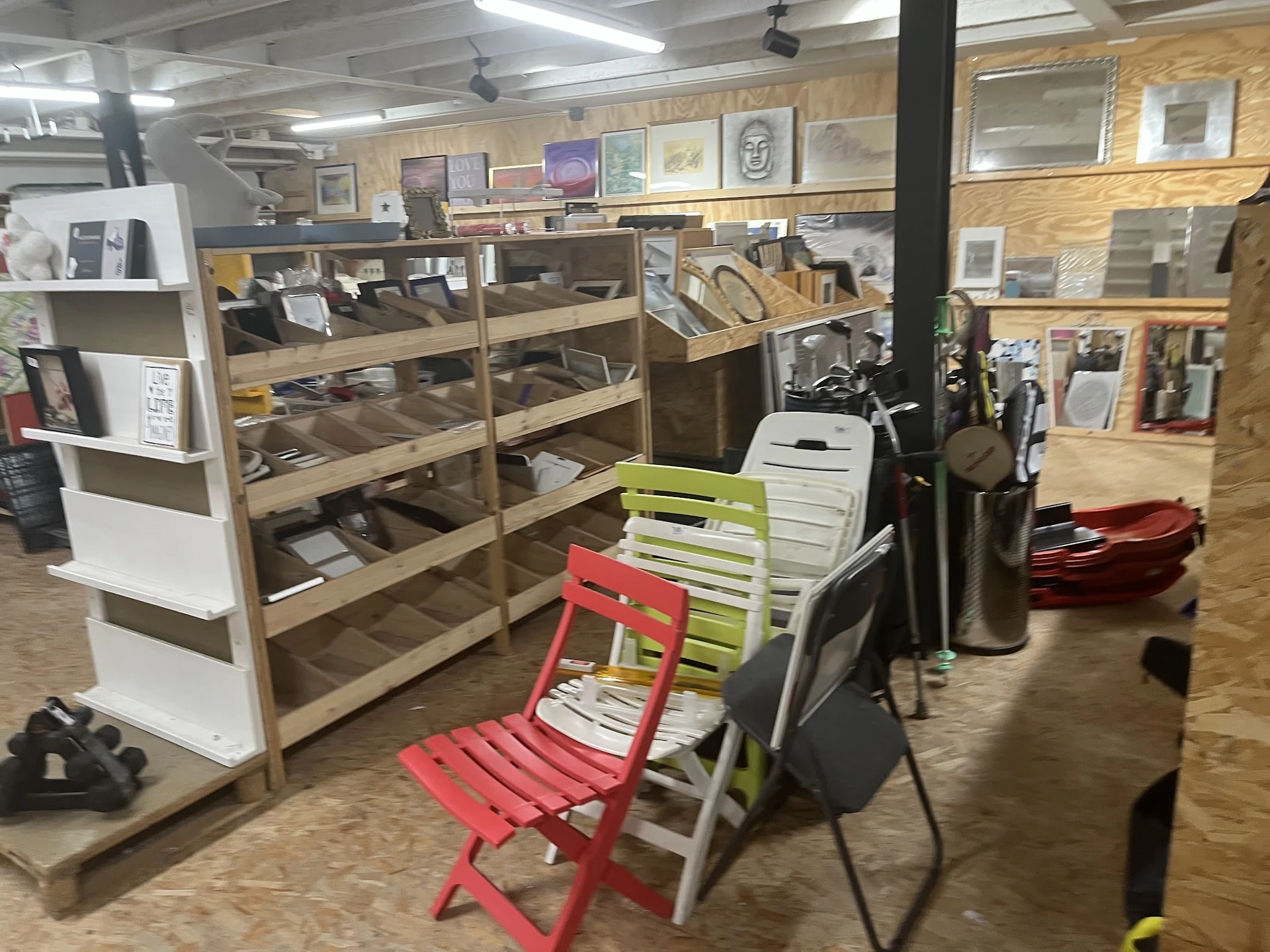 Winkelvloer met houten stellingen vol artikelen, rode en gele stoelen, en diverse meubels en spullen