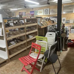 Winkelvloer met houten stellingen vol artikelen, rode en gele stoelen, en diverse meubels en spullen