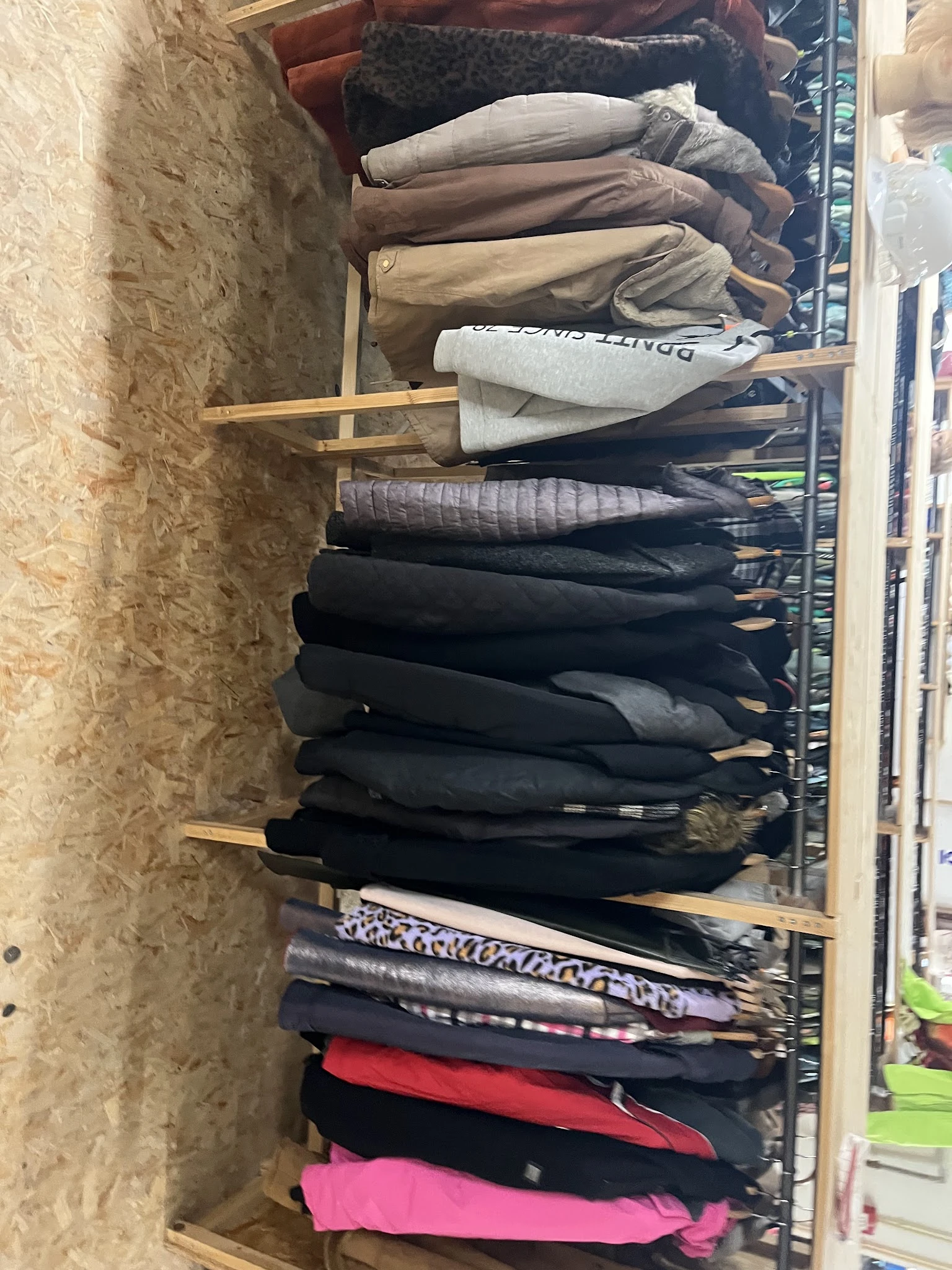 Stapel tweedehands jassen en jasjes op een houten rek in de winkel