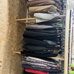 Stapel tweedehands jassen en jasjes op een houten rek in de winkel