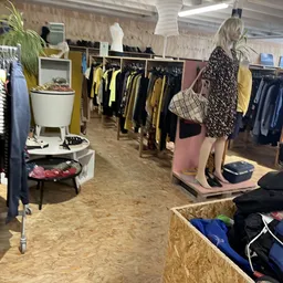 Winkelvloer met kledingrekken en uitgestalde tweedehands kleding in verschillende kleuren