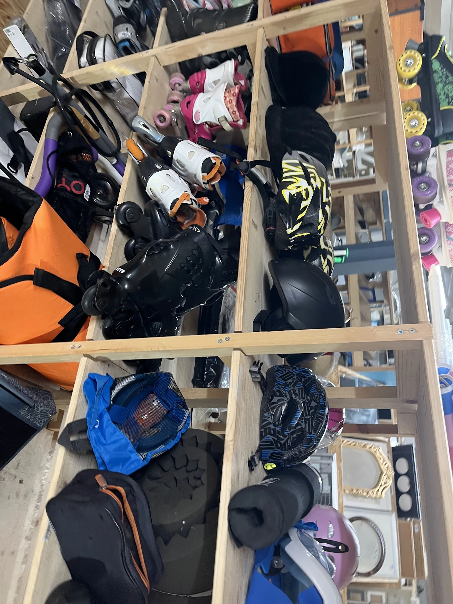Houten kastje met vakken vol sportuitrusting: helmen, beschermingsmateriaal en sportkleding in zwart, blauw en oranje