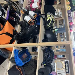 Houten kastje met vakken vol sportuitrusting: helmen, beschermingsmateriaal en sportkleding in zwart, blauw en oranje