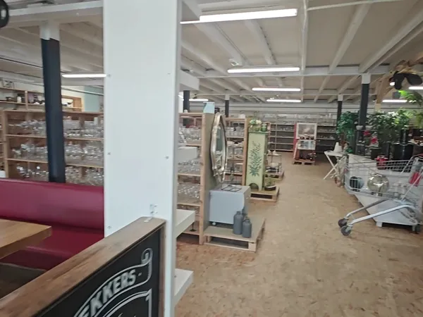 Binnenaanzicht van kringloopwinkel met stellingen, rekken met spullen, winkelwagen en zithoek met rode bank