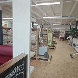 Winkelvloer van kringloopwinkel met stellingen, tafels, plantenbak en diverse artikelen