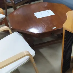 Bruine houten eettafel met blad en onderblad, met witte stoelen ernaast