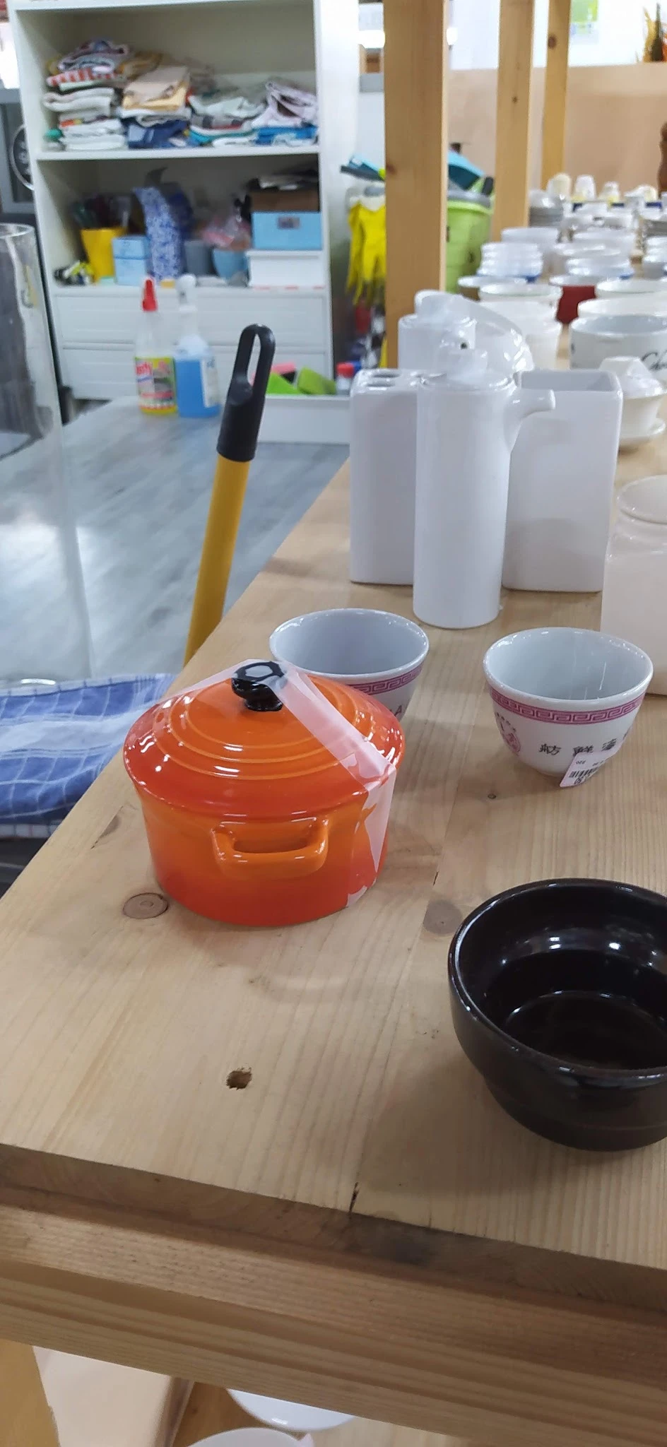 Oranje gesloten braadpan met zwarte knop op houten tafel naast twee decoratieve kopjes en witte containers
