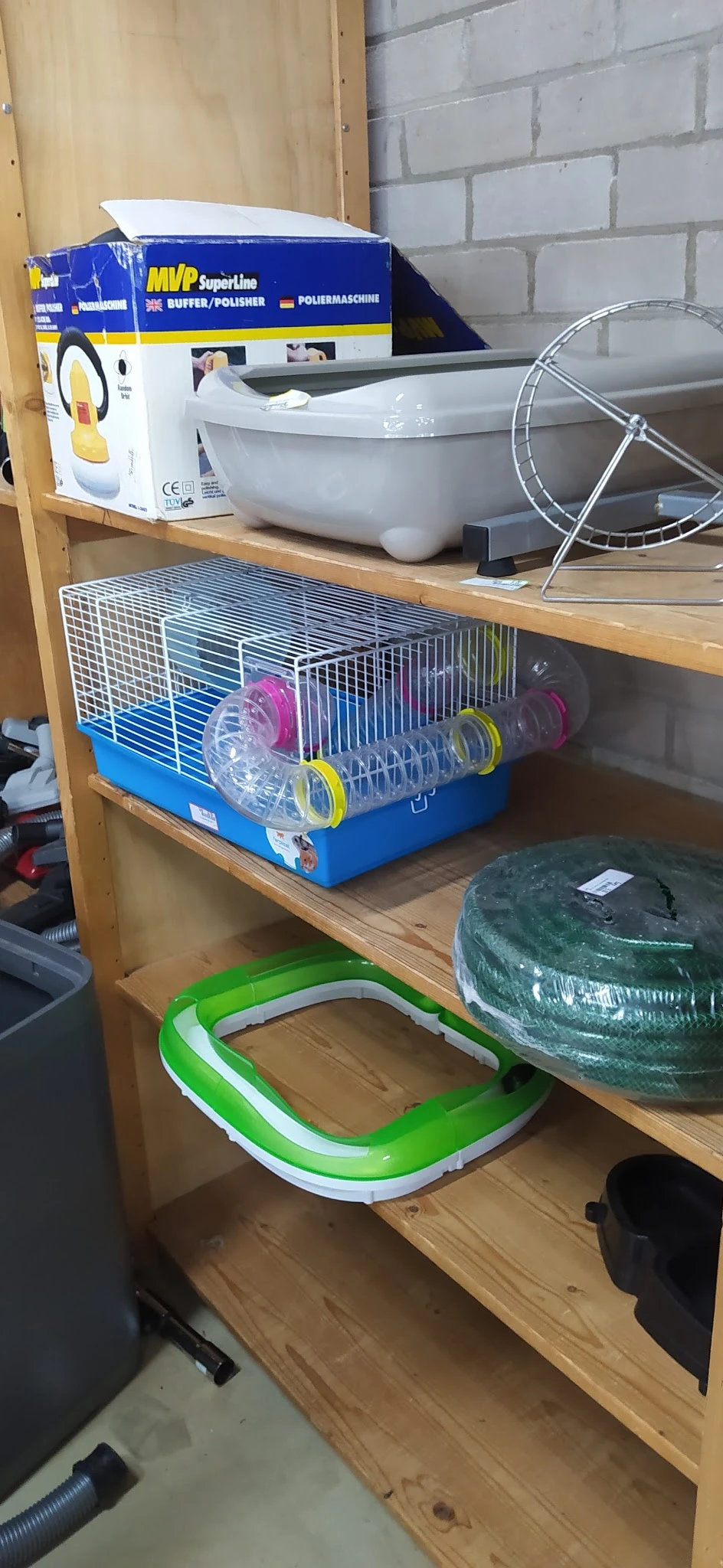 Kleine knaagdierkooi met roze en gele accessoires op een houten plank in een winkelrek