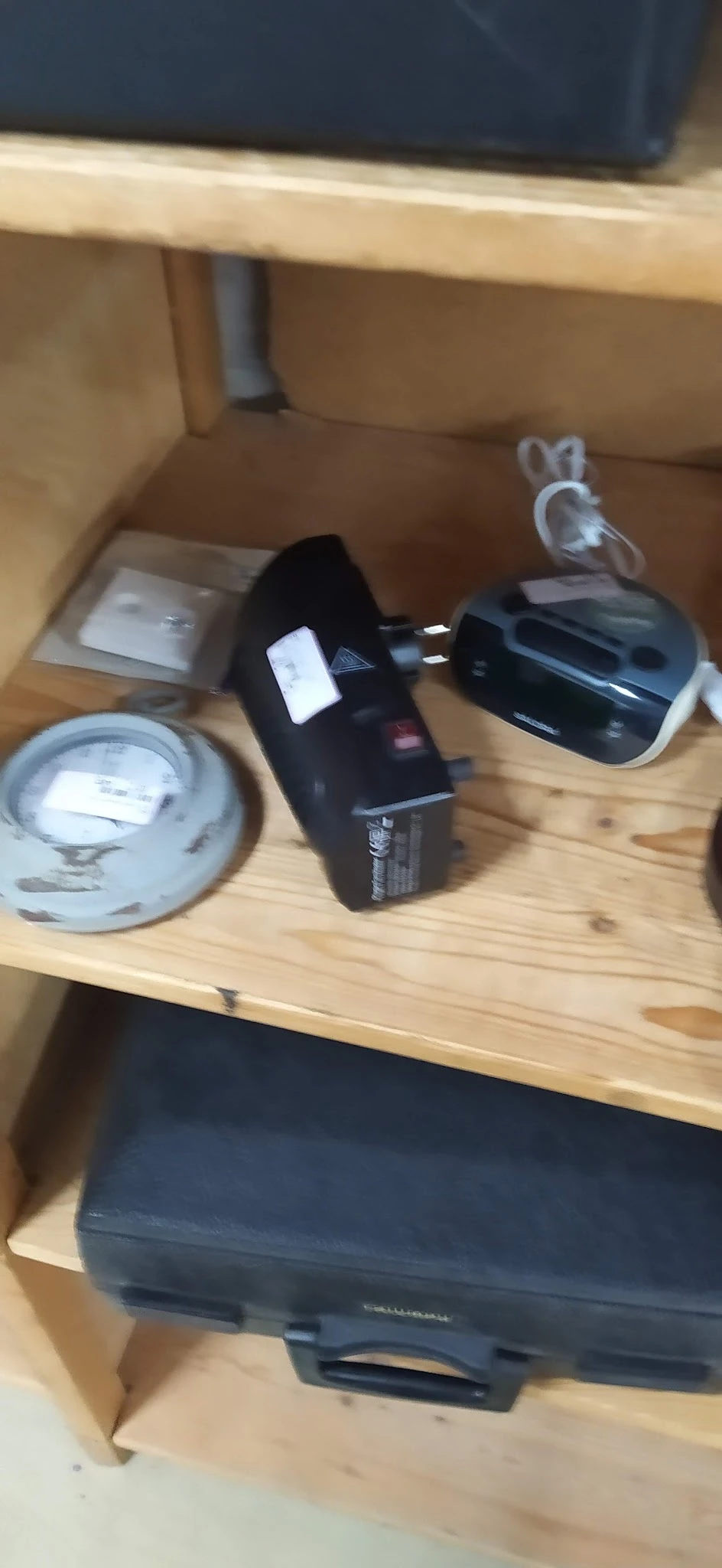 Diverse elektronica en huishoudelijke artikelen op een houten tafel, waaronder een stroomadapter, zwarte apparaten en plastic