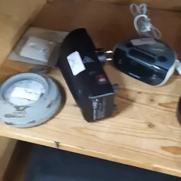 Diverse elektronica en huishoudelijke artikelen op een houten tafel, waaronder een stroomadapter, zwarte apparaten en plastic