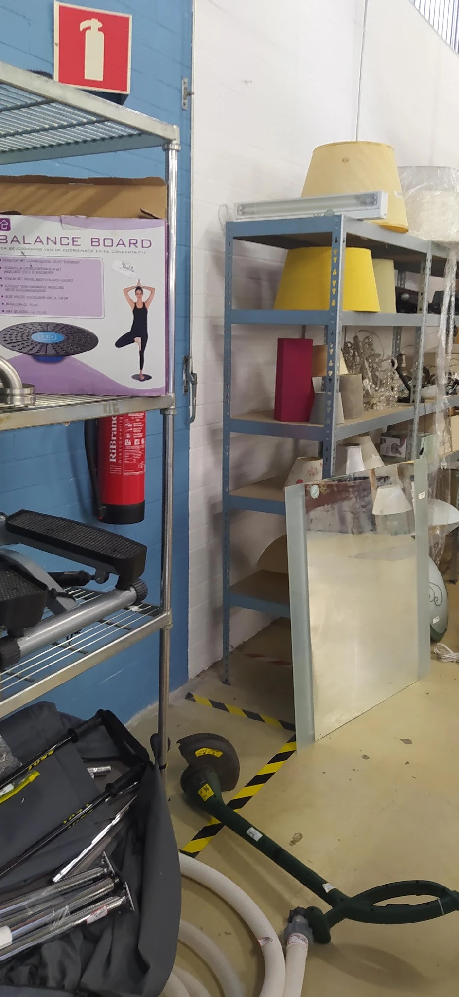 Winkelinterieur met blauwe stellingen, rode brandblusser en diverse spullen op planken