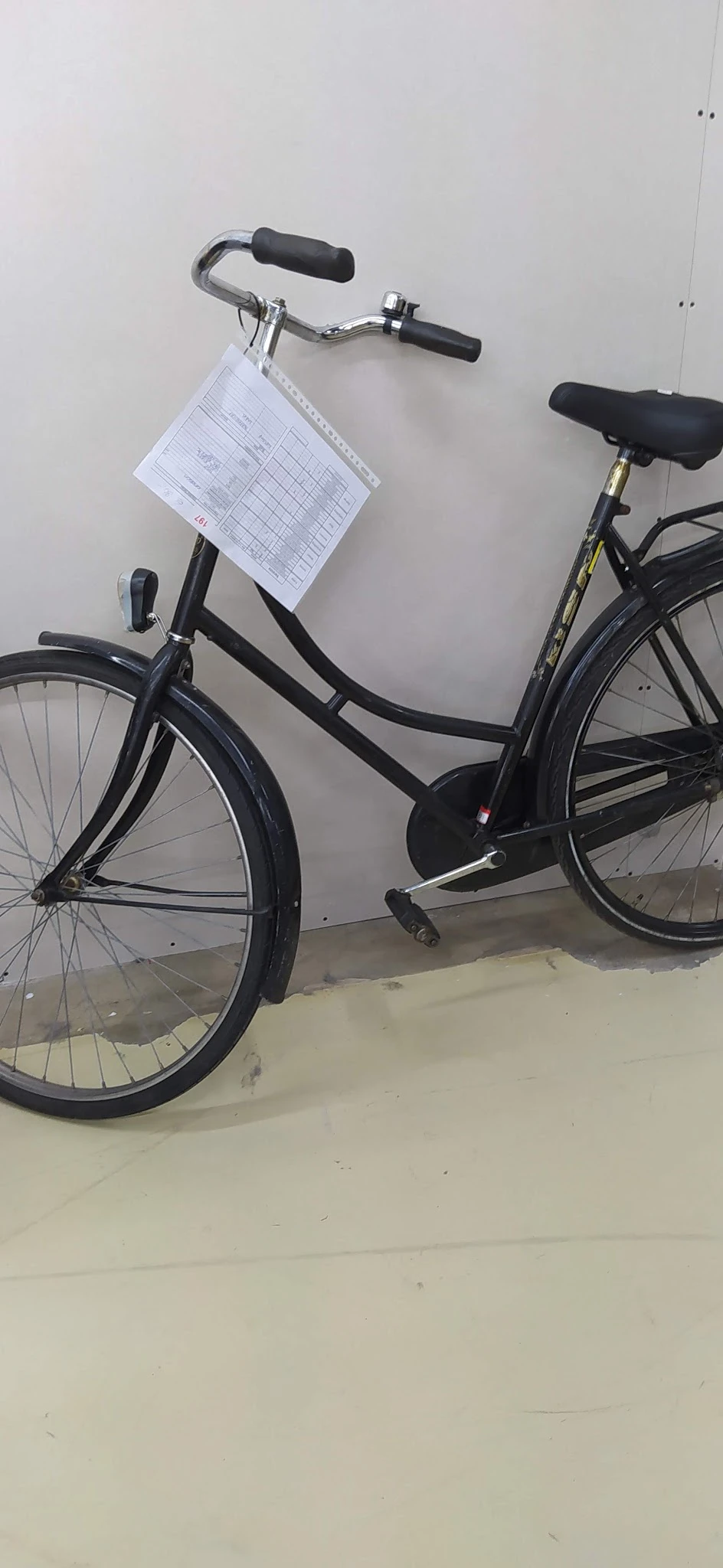 Zwarte damesfiets met kettingkast tegen witte muur, schuin van voren gefotografeerd