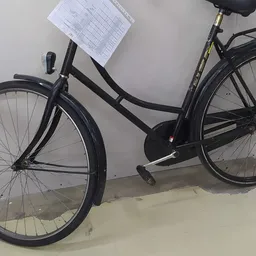 Zwarte damesfiets met kettingkast tegen witte muur, schuin van voren gefotografeerd