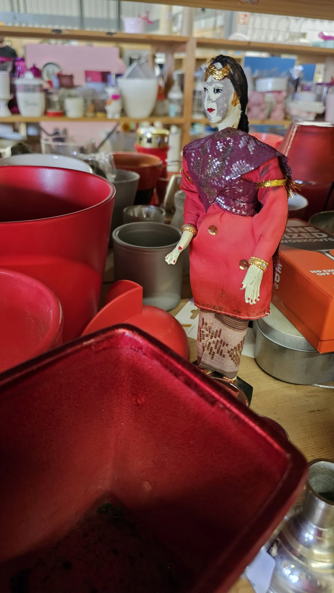 Verzameling tweedehands items waaronder rode en roze tassen, serviesgoed en decoratiespullen op display