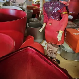 Verzameling tweedehands items waaronder rode en roze tassen, serviesgoed en decoratiespullen op display