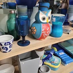 Tafel met diverse items: blauwe glazen, een decoratieve uil, flessen en kopjes met blauwe patronen.