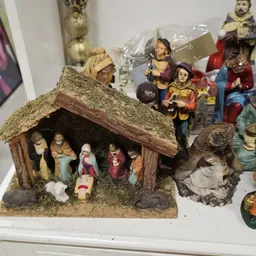 Kerststalletje met houten dak en figuren van Maria, Jozef en kind Jezus, naast decoratiefiguren