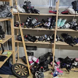 Houten stellingen vol met tweedehands sportuitrusting en beschermingsmateriaal, waaronder helmen, pads en skates