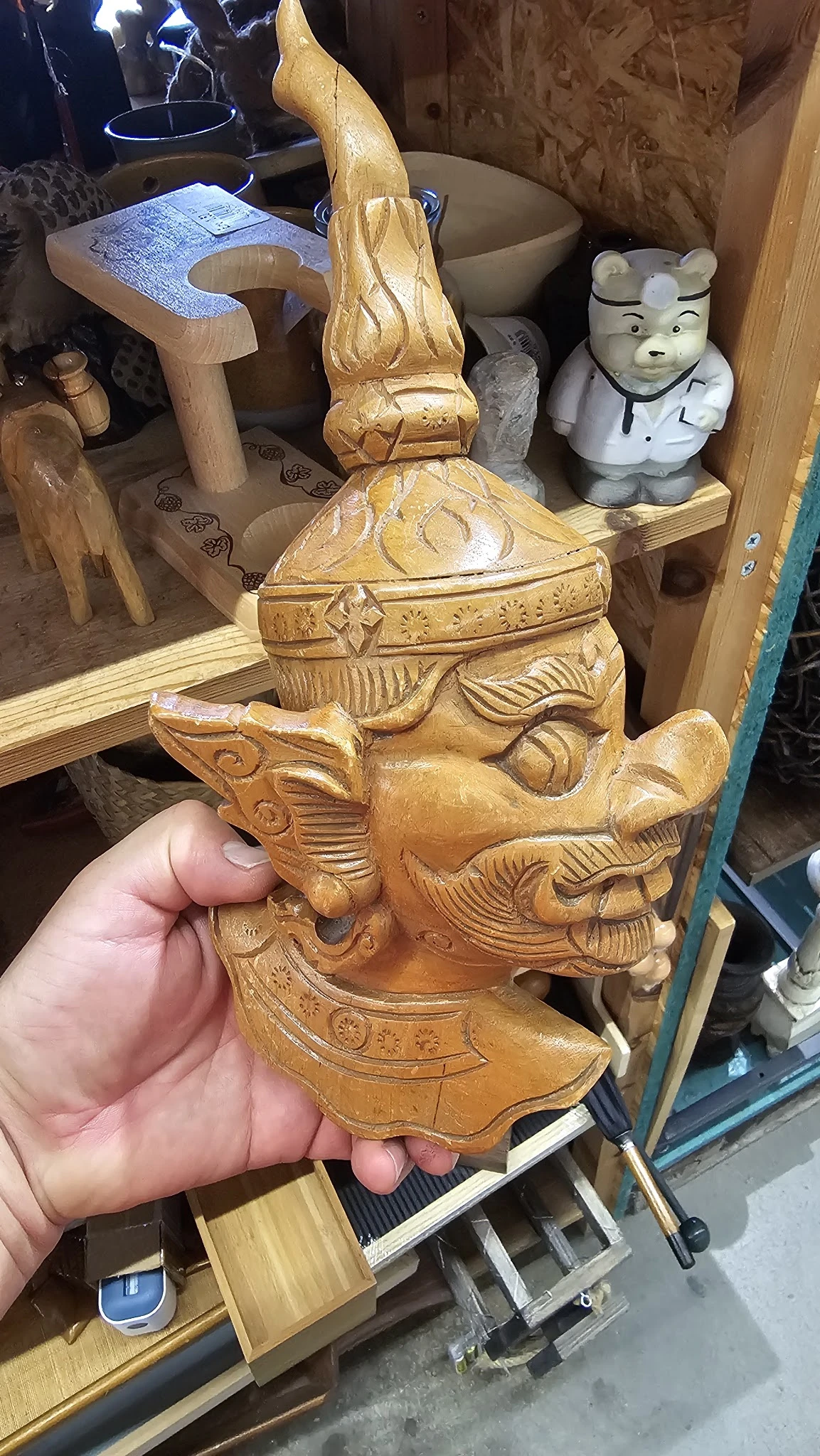 Houten beeldhouwwerk van een Aziatisch gezicht met decoratieve details, in hand gehouden