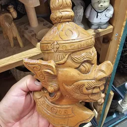 Houten beeldhouwwerk van een Aziatisch gezicht met decoratieve details, in hand gehouden