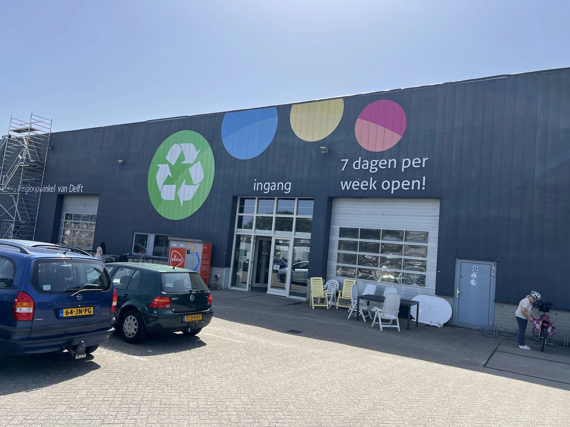 Zwarte gevel van kringloopwinkel met gekleurde cirkels en ingang, parkeerplaats ervoor