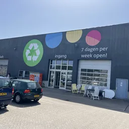 Zwarte gevel van kringloopwinkel met gekleurde cirkels en ingang, parkeerplaats ervoor