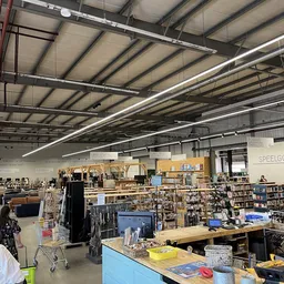 Ruim magazijn met houten stellingen vol spullen, tafels met artikelen en klanten aan het winkelen