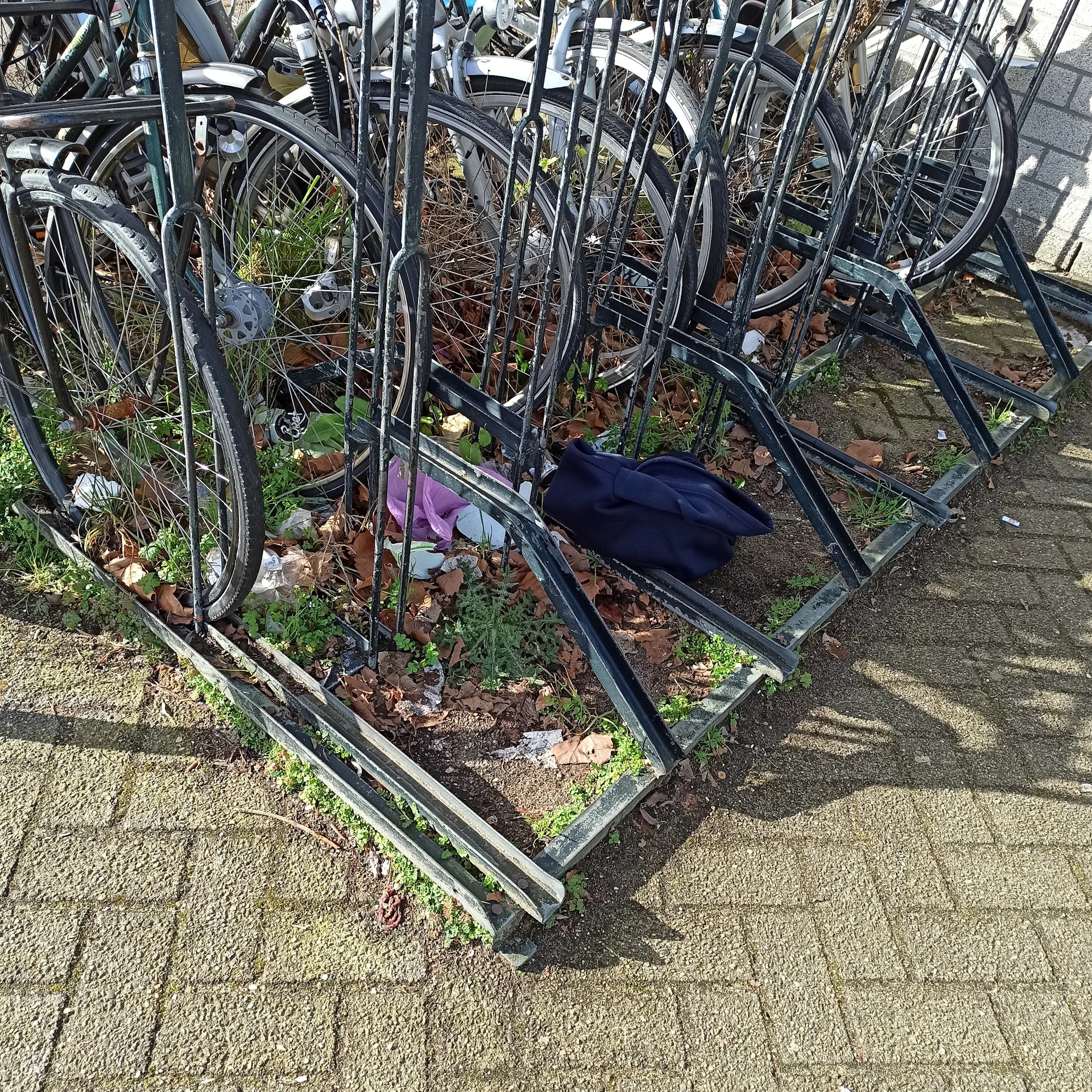 Fietsen in een fietsenrek met grond en bladeren, één fiets omgevallen