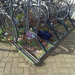 Fietsen in een fietsenrek met grond en bladeren, één fiets omgevallen