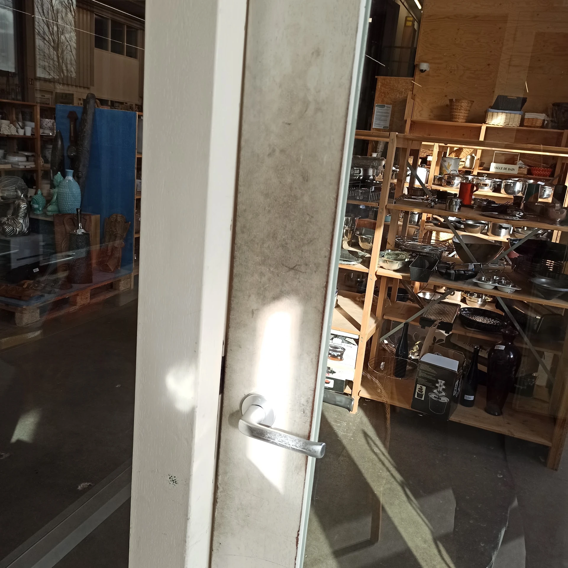 Zicht op glazen deur en winkelinterieur met houten stellingen en spullen op achtergrond