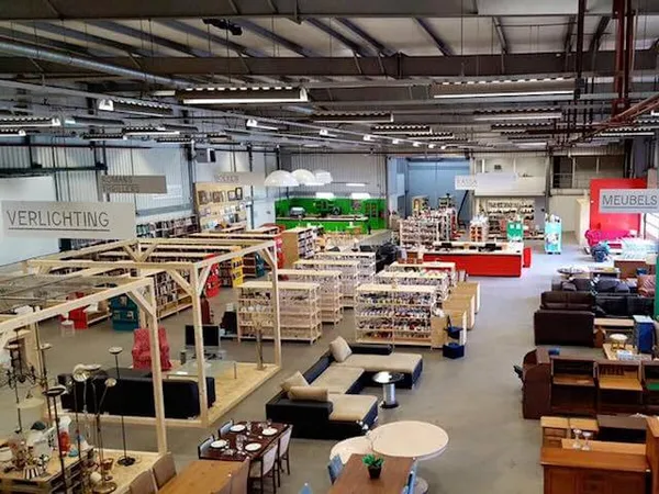 Overzicht van kringloopwinkel met houten stellingen, meubelstukken, huishoudspullen en diverse tweedehands artikelen versprei