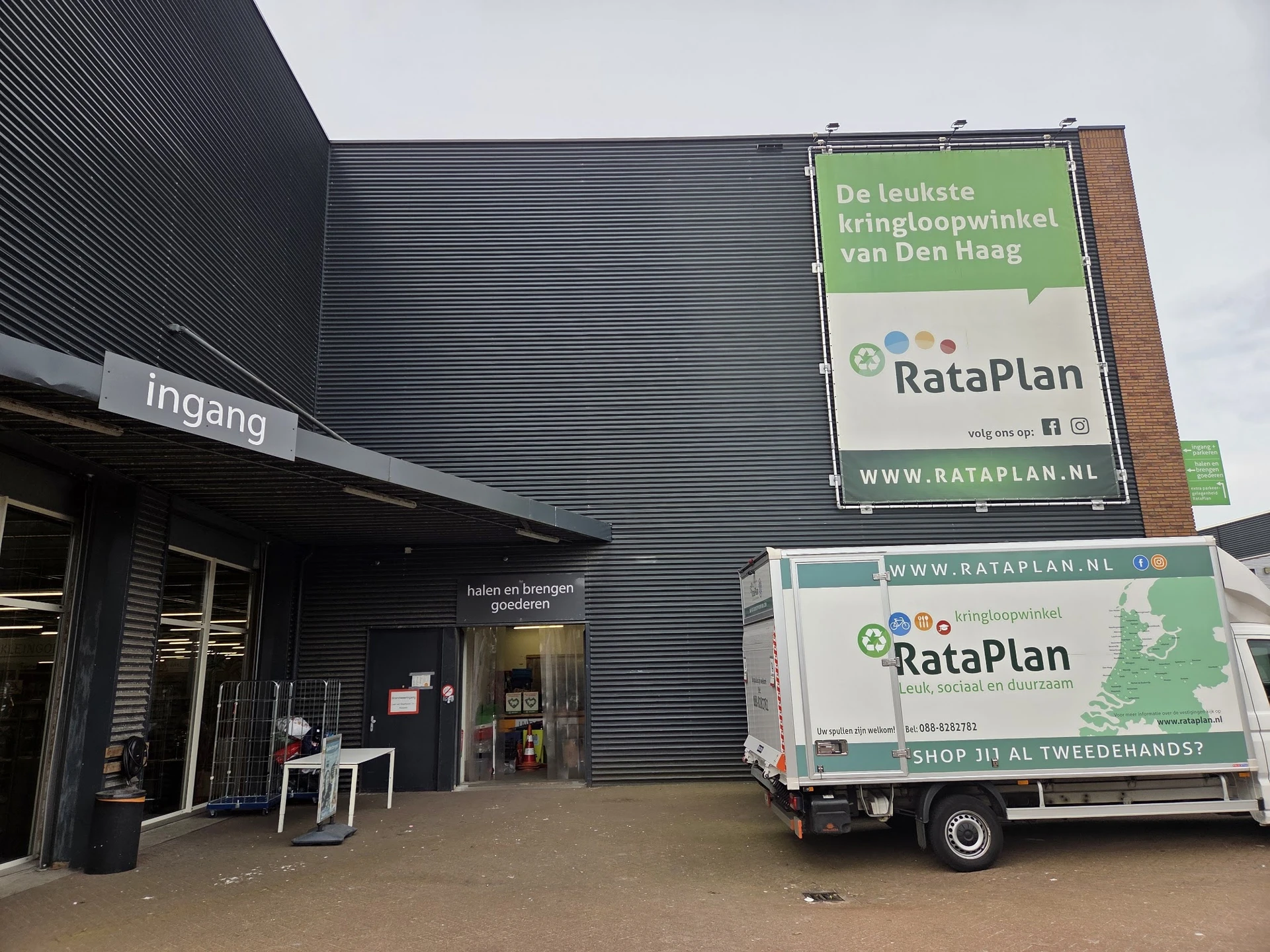 Voorkant kringloopwinkel met ingang, donkergrijze gevel en RataPlan borden. Bedrijfsbus geparkeerd ervoor.