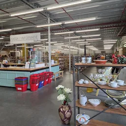 Overzicht van kringloopwinkel met kassabalie, stellingen met servies en huishoudwaar, rode kratten en wit beschilderde zuilen