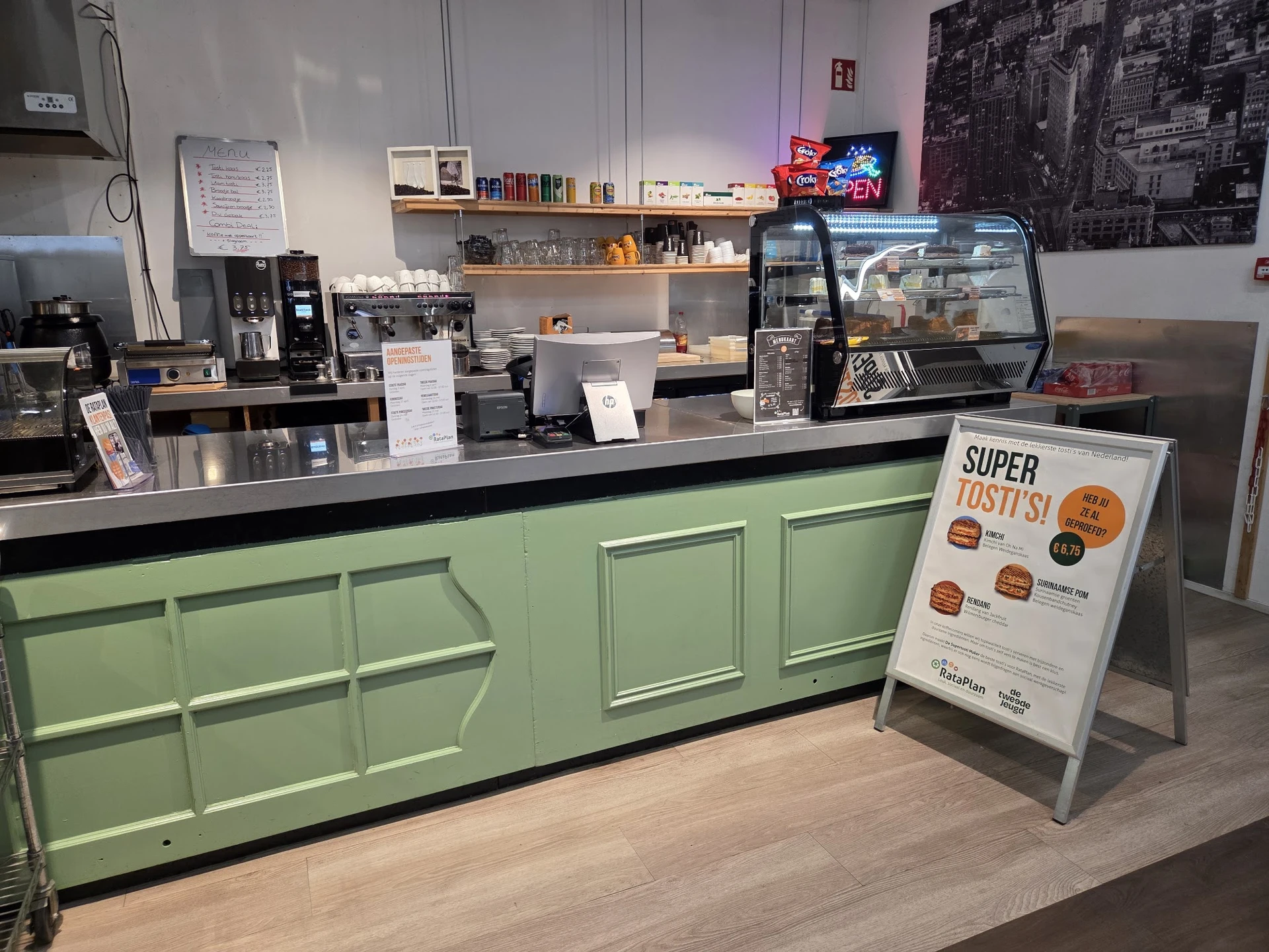Toonbank van koffiehoek met groene kasten, koffieapparaat en 'Super Tosti' menukaart