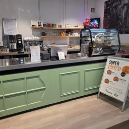 Toonbank van koffiehoek met groene kasten, koffieapparaat en 'Super Tosti' menukaart