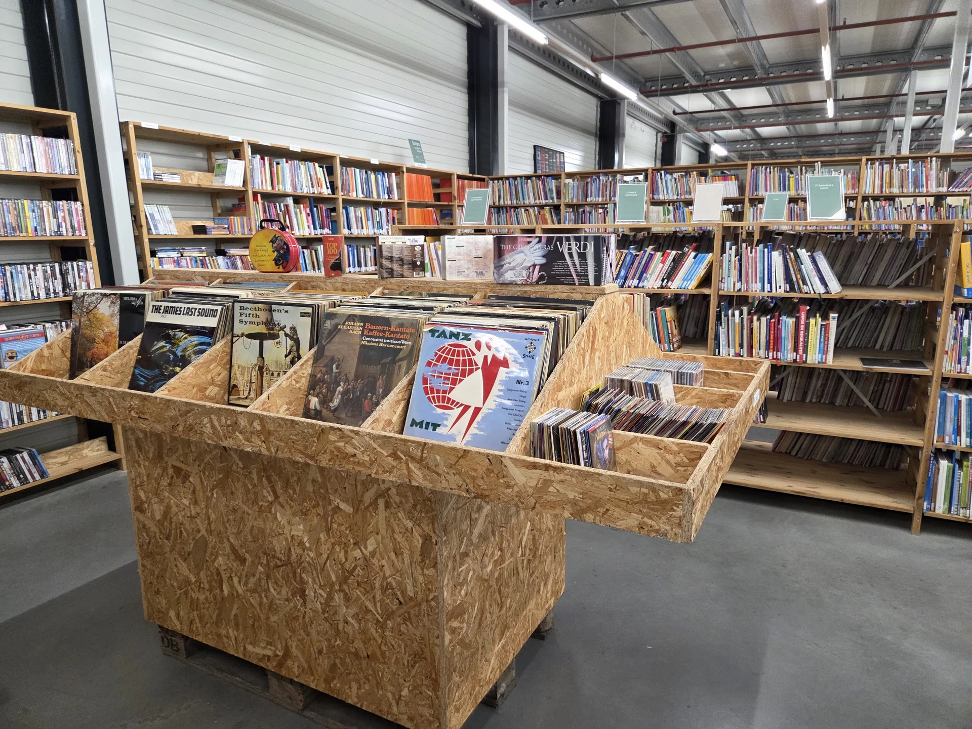 Winkelvloer met houten display-kastjes vol met boeken en media, schappen met boeken op de achtergrond