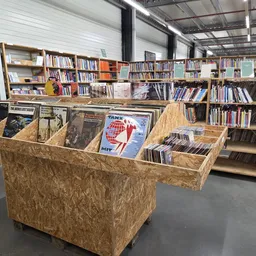 Winkelvloer met houten display-kastjes vol met boeken en media, schappen met boeken op de achtergrond