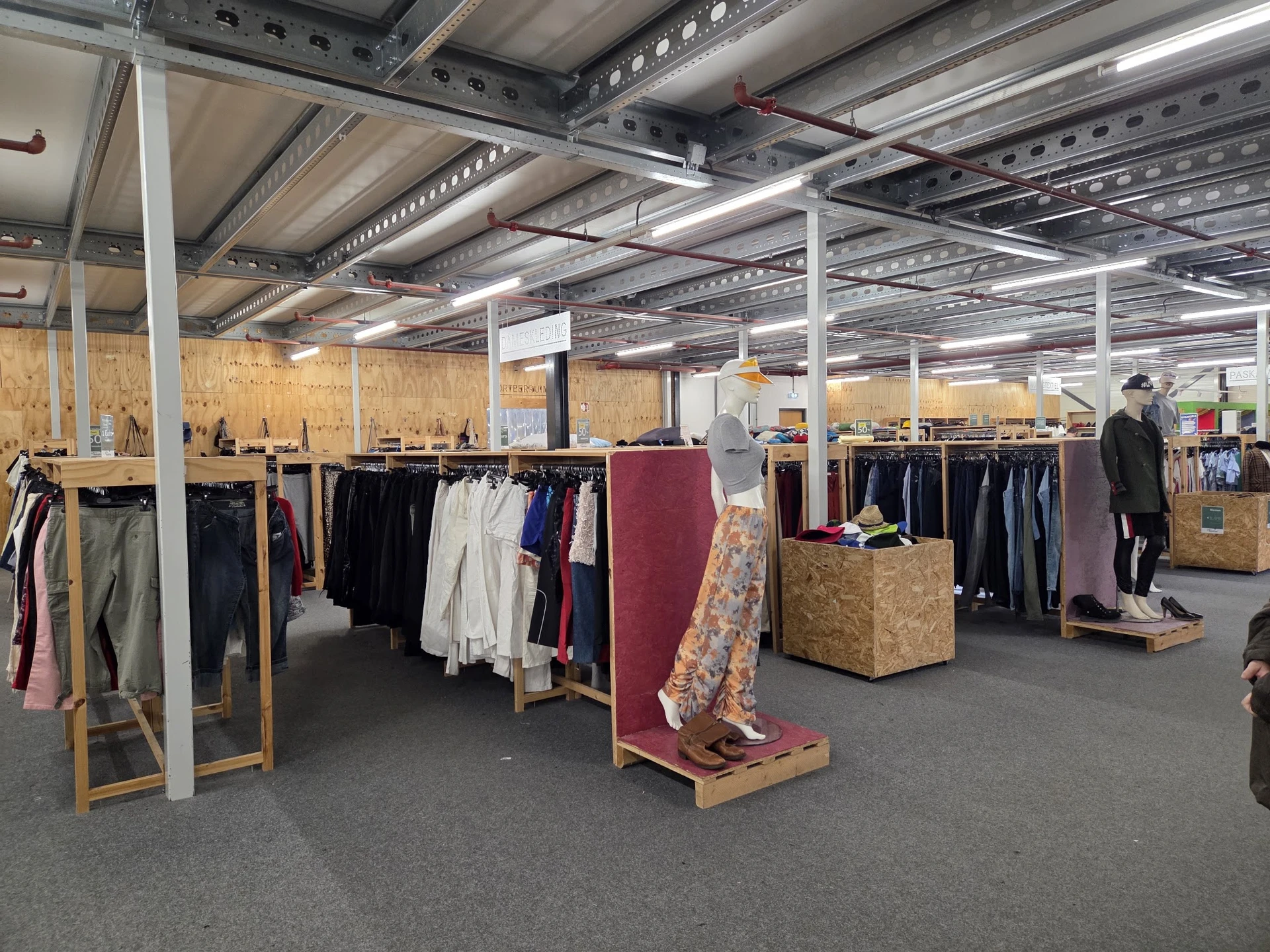 Ruime winkelhal met kledingrekken, spiegels en houten displays, LED-verlichting aan plafond