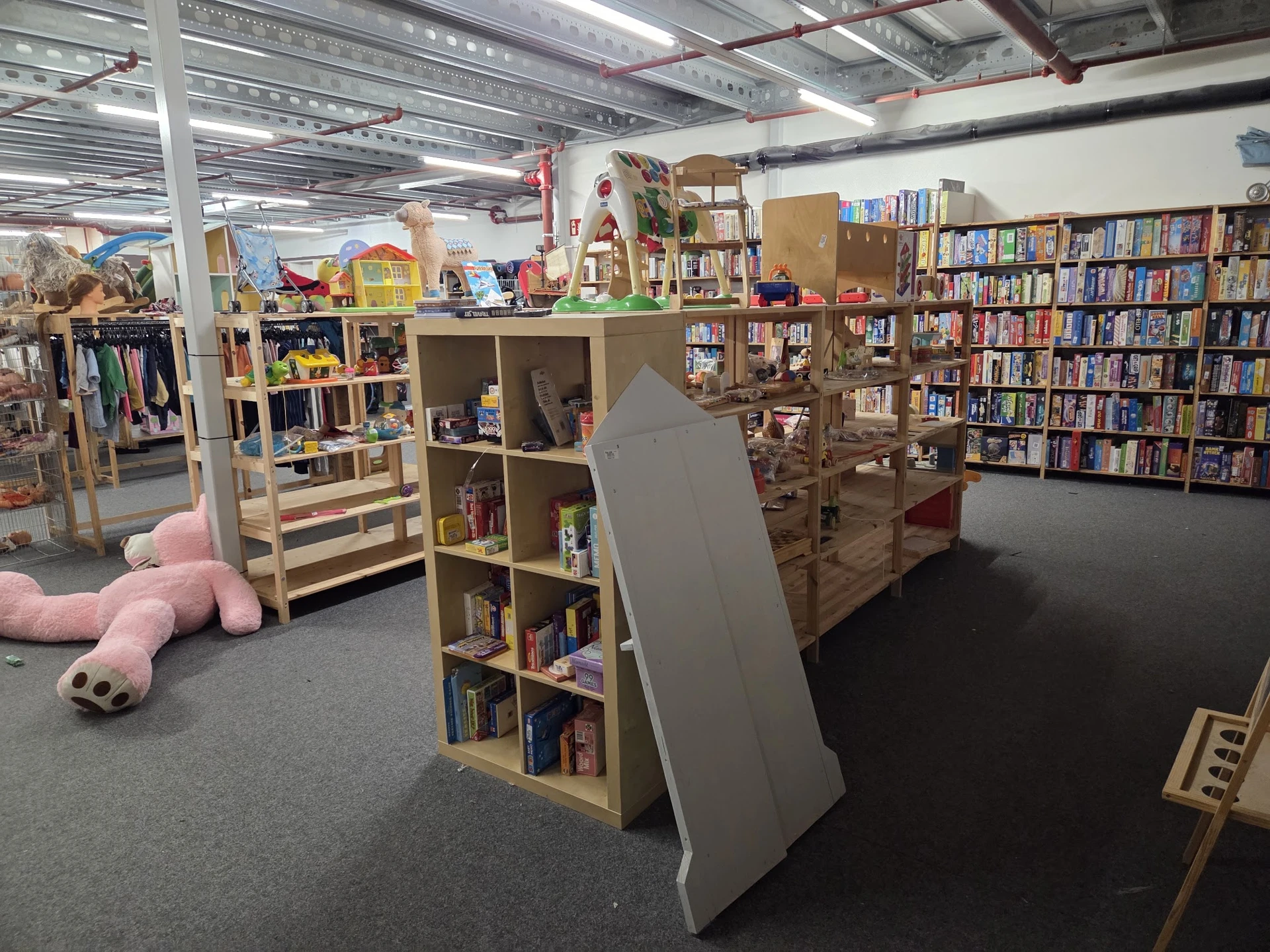 Binnenkant van kringloopwinkel met boekenkasten, speelgoed en diverse goederen op stellingen en vloer