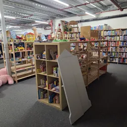 Binnenkant van kringloopwinkel met boekenkasten, speelgoed en diverse goederen op stellingen en vloer