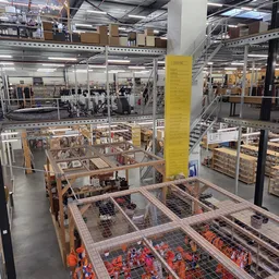 Meerdere verdiepingen van een kringloopwinkel met stellingen, opgeslagen spullen en een opvallende gele zuil in het midden