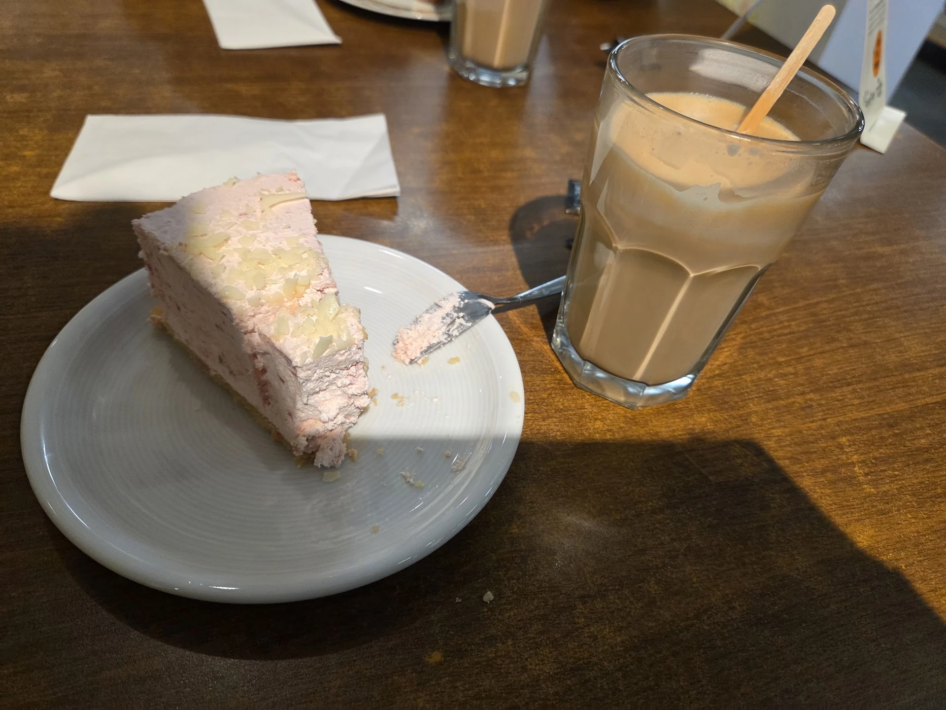 Bord met stuk cake en glas met bruin drankje op houten tafel in lunchroom